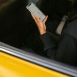 Kobieta w żółtej taksówce korzysta ze smartfona do nawigacji